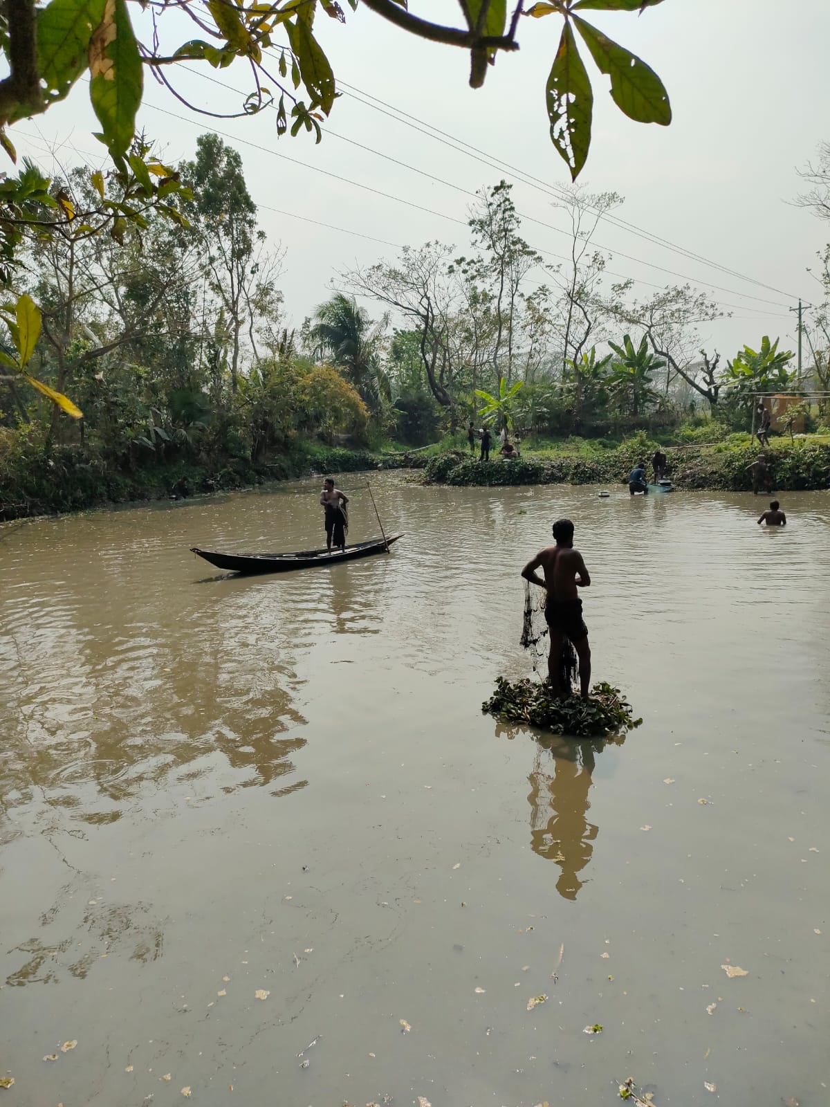 Fishermen casting nets on a tranquil village canal with lush greenery in the background